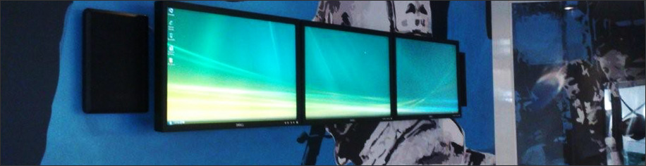 Three LCD screens mounted on a wall with speakers